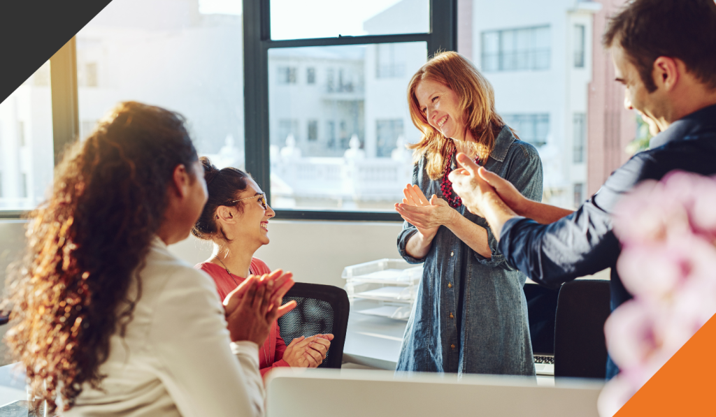 three employees gathered around a fourth employee experiencing the power of recognition