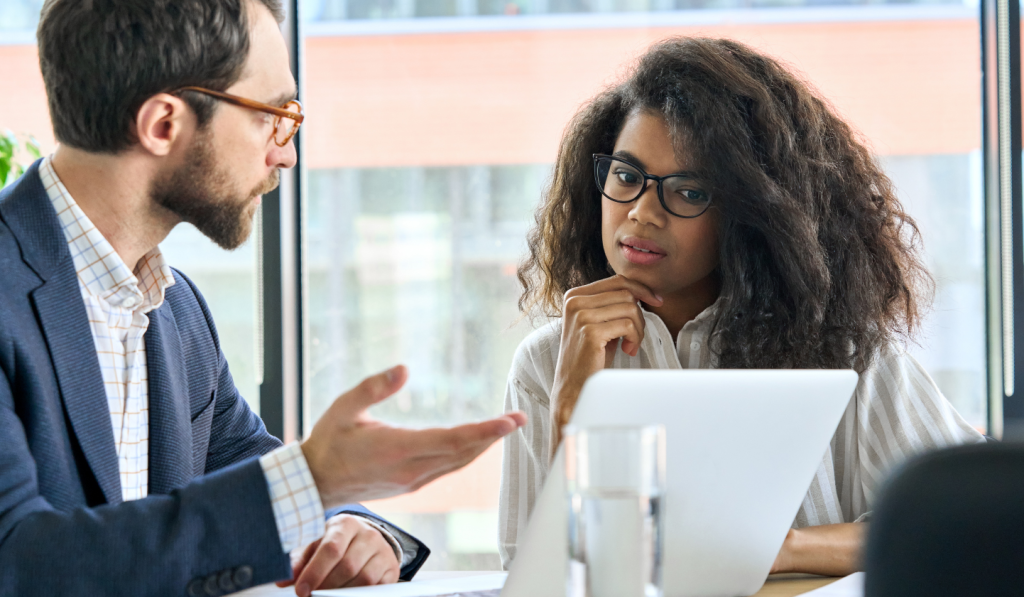 a male coworker is speaking with a female coworker at a desk focusing on how to stop micromanaging a team